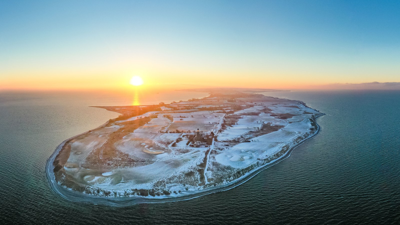 Luftfoto af Vestærø, fyr og golfbane med sne og solnedgang